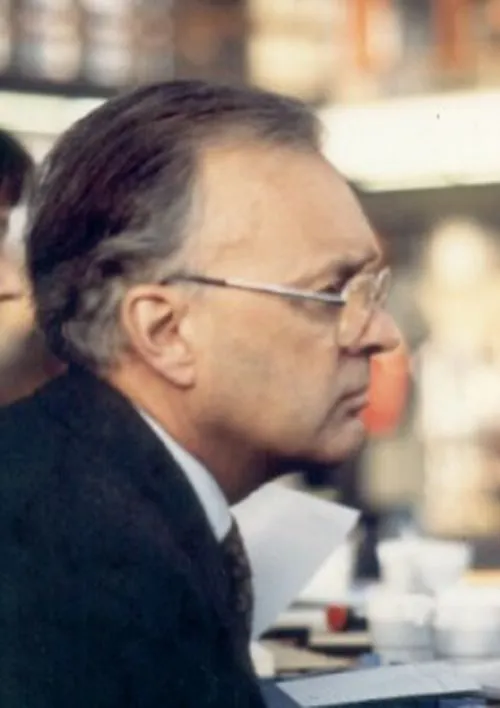 Colour photo of an older man in glasses and a dark suit, seen in profile.